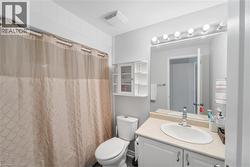 Bathroom featuring a single vanity with an oval sink, a wall-mounted mirror with overhead light bar, a toilet, and a built-in wall cabinet with shelving - 