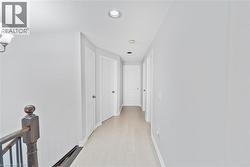 Bright hallway featuring light wood-finish flooring, recessed lighting, and white paneled doors - 