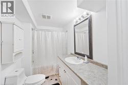 Bathroom featuring a single vanity with an integrated sink, a large framed mirror, a wall-mounted light fixture with four bulbs, a toilet, and a combination shower/tub with a shower rod - 