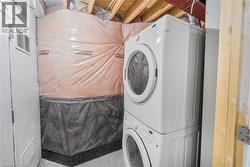 Laundry area featuring a stacked washer and dryer unit, exposed ceiling joists, and a partially finished wall with insulation - 