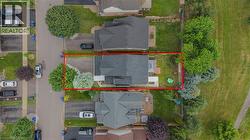 Aerial perspective showcasing a residential property with a dark shingled roof, bordered by a paved roadway and a grassy area - 