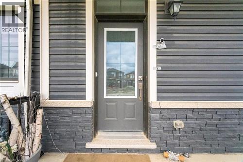 Entry door with upper glass panel, dark gray siding, stone-finish foundation, light-colored trim, and an exterior light fixture - 240 Velvet Way, Niagara Falls, ON - Outdoor