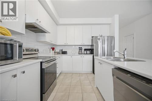 Contemporary kitchen featuring white cabinetry, stainless steel appliances, a double basin sink, light-toned tile flooring, and a subway tile backsplash - 240 Velvet Way, Niagara Falls, ON - Indoor Photo Showing Kitchen With Double Sink