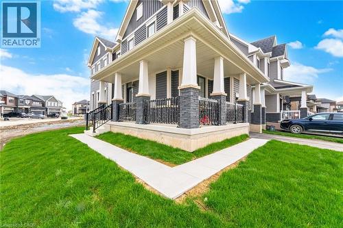 Exterior featuring dark siding with white trim, a covered front porch with stone-clad columns, a black wrought iron railing, and a concrete walkway - 240 Velvet Way, Niagara Falls, ON - Outdoor With Facade