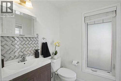 Bathroom featuring a wood-finish vanity with an integrated sink, a herringbone pattern tile backsplash, and a framed mirror - 60 Postmaster Drive, Kitchener, ON - Indoor Photo Showing Bathroom