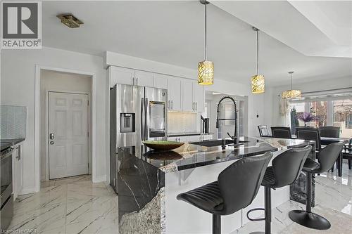 Spacious kitchen with a waterfall island featuring dark countertops, modern pendant lighting, white cabinetry, stainless steel appliances, and large format marble-look floor tiles - 60 Postmaster Drive, Kitchener, ON - Indoor Photo Showing Other Room