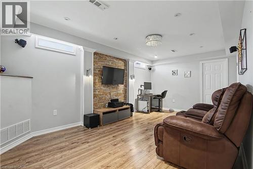 Recreation room featuring wood-finish flooring, a stacked stone accent wall, recessed lighting, and a crystal chandelier - 60 Postmaster Drive, Kitchener, ON - Indoor