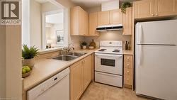Kitchen featuring light wood-finish cabinetry, white appliances, and a double basin stainless steel sink. Virtually Staged - 