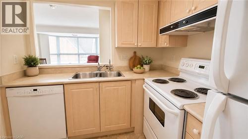 Functional kitchen featuring a double basin stainless steel sink, light wood-finish cabinetry, and a pass-through window. Virtually Staged. - 20 St. George Street Unit# 404, Kitchener, ON - Indoor Photo Showing Kitchen With Double Sink