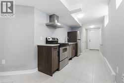 Galley kitchen featuring stainless steel appliances, wood-finish cabinetry, light-toned countertops, and tile flooring - 