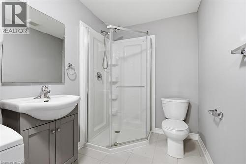 Bathroom featuring a glass-enclosed shower, white ceramic toilet, vanity with a white basin and gray cabinetry, rectangular wall-mounted mirror, and tile flooring - 3 Hagar Street, Thorold, ON - Indoor Photo Showing Bathroom