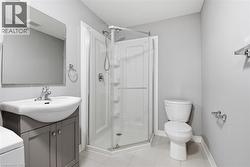 Bathroom featuring a glass-enclosed shower, white ceramic toilet, vanity with a white basin and gray cabinetry, rectangular wall-mounted mirror, and tile flooring - 