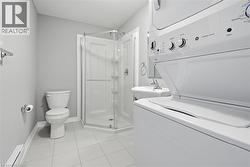Compact bathroom featuring a corner glass-enclosed shower, pedestal sink, and a stacked washer and dryer unit - 