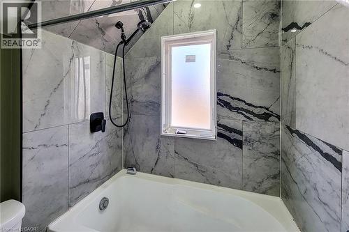 Bathtub and shower combination featuring floor-to-ceiling marbled tile, a frosted window, and matte black fixtures - 334 Gage Avenue N, Hamilton, ON - Indoor Photo Showing Bathroom