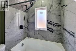 Bathtub and shower combination featuring floor-to-ceiling marbled tile, a frosted window, and matte black fixtures - 