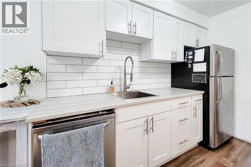 Modern kitchen featuring white shaker cabinetry with brushed nickel hardware, light-toned countertops, a subway tile backsplash, stainless steel sink with a gooseneck faucet, and a stainless steel ref - 7 Davidson Boulevard Unit# 14, Dundas, ON - Indoor Photo Showing Kitchen With Upgraded Kitchen