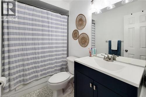 Bathroom featuring a vanity with a white countertop and dark blue cabinetry, a wall-mounted mirror, a toilet, a full shower with a tub, and light-toned flooring - 7 Davidson Boulevard Unit# 14, Dundas, ON - Indoor Photo Showing Bathroom