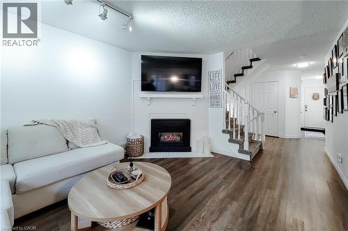 Living area featuring dark wood-finish flooring and a white brick fireplace with a black insert - 7 Davidson Boulevard Unit# 14, Dundas, ON - Indoor Photo Showing Living Room With Fireplace