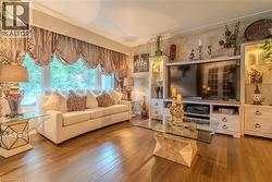 Living area featuring wood-finish flooring, a large picture window with custom window treatments, and built-in media cabinetry with display shelving - 
