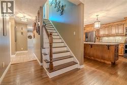Hardwood flooring extending from the entryway into the kitchen, featuring a staircase with white risers and dark wood treads - 