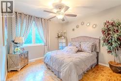 Bedroom featuring a large window with patterned drapes, a ceiling fan with integrated lighting, and parquet wood-finish flooring - 