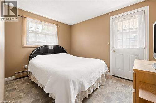 Bedroom featuring a paneled exterior door with window, a single window, baseboard heating, and stone-look flooring - 162 Tiffany Street, Cambridge, ON - Indoor Photo Showing Bedroom