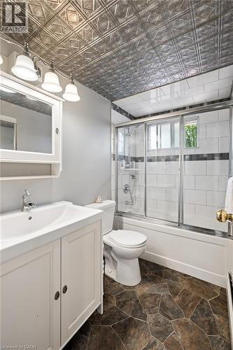 Bathroom featuring a decorative metallic ceiling, a white vanity with integrated sink, a full bath with sliding glass doors, white subway tile surround with accent band, and irregular stone-look floor - 162 Tiffany Street, Cambridge, ON - Indoor Photo Showing Bathroom