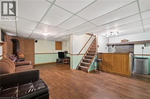 Finished lower level featuring wood-finish flooring, a brick accent wall with a wood-burning stove, a built-in wet bar, and a drop panel ceiling with flush-mount lighting - 162 Tiffany Street, Cambridge, ON - Indoor