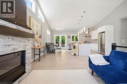 Expansive open-concept living space featuring a stacked stone fireplace with a substantial wood mantel, vaulted ceilings with transom windows, and light wood-finish flooring - 