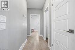 Hallway featuring light wood-finish flooring, light grey painted walls, white trim, and white panel doors with contemporary hardware - 