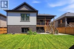 Rear exterior featuring a covered deck with wood railings, a concrete patio, and a manicured lawn - 