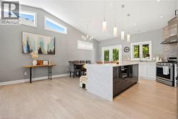 Open-concept kitchen and dining area featuring a waterfall kitchen island with integrated appliances, stainless steel range with hood, white cabinetry, and light wood-finish flooring - 