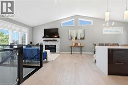 Spacious living area featuring light wood-finish flooring, a stone-clad fireplace, and a vaulted ceiling with triangular windows - 