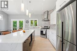 Modern kitchen featuring an expansive island with a waterfall countertop, sleek white cabinetry, stainless steel appliances, and a mosaic tile backsplash - 
