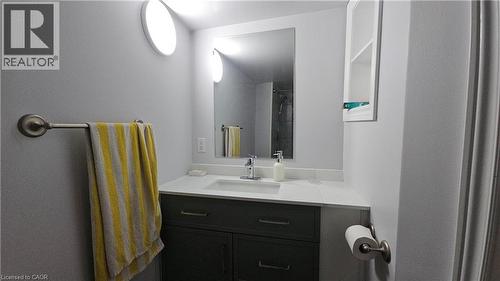 Bathroom vanity featuring a single sink with a chrome faucet, light-toned countertop, and dark cabinetry - 10 Doll Court, Kitchener, ON - Indoor Photo Showing Bathroom