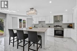 Modern kitchen featuring white cabinetry, a large center island with a speckled countertop, integrated stainless steel appliances, a white subway tile backsplash, and polished marble-look flooring - 