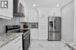 Contemporary kitchen featuring white cabinetry, stone countertops, stainless steel appliances, a subway tile backsplash, and large format floor tiles - 