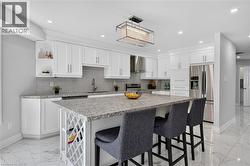 Kitchen featuring a central island with integrated wine rack, light-toned countertops, white cabinetry with crown molding, stainless steel appliances, and marble-look tile flooring - 