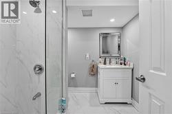 Bathroom featuring a glass-enclosed shower with white marble-look tile, a white vanity with an integrated sink, a rectangular framed mirror, recessed lighting, and a white paneled door - 