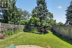 Expansive backyard featuring a lush lawn, perimeter wood fencing, mature trees, and multiple raised garden beds - 