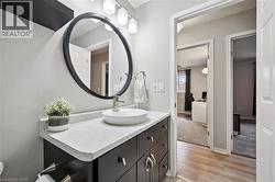 Modern bathroom featuring a dark wood-finish vanity with a vessel sink, a circular mirror with a black frame, and a three-light vanity fixture - 