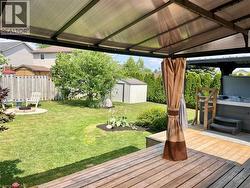 Expansive backyard featuring a wood-finish deck with a covered patio structure, a hot tub, a manicured lawn, a fire pit, and a storage shed - 