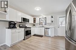 Kitchen featuring white cabinetry, light-toned countertops, stainless steel appliances, wood-finish flooring, and a rear exterior door - 