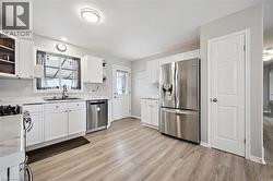 Contemporary kitchen featuring white cabinetry, stainless steel appliances, wood-finish flooring, and a window over the sink - 