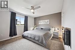 Carpeted bedroom featuring a window with dark curtains, a ceiling fan with integrated lighting, a contrasting accent wall, and white trim - 