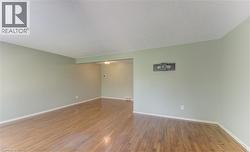 Spacious interior room featuring light-toned walls, wood-finish flooring, white baseboards, and a textured ceiling - 