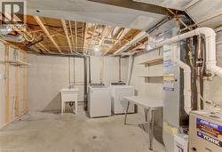 Basement laundry area featuring a utility sink, washer and dryer connections, exposed ceiling joists, concrete flooring, and unfinished walls - 