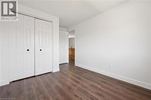 Interior room featuring wood-finish flooring, white walls, and white bi-fold closet doors with black hardware - 71 Peach Blossom Crescent, Kitchener, ON - Indoor Photo Showing Other Room