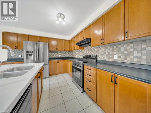 Kitchen featuring abundant wood cabinetry, stainless steel appliances, dark countertops, a mosaic tile backsplash, and white tile flooring - 39 Baintree Way, Cambridge, ON - Indoor Photo Showing Kitchen With Stainless Steel Kitchen With Double Sink
