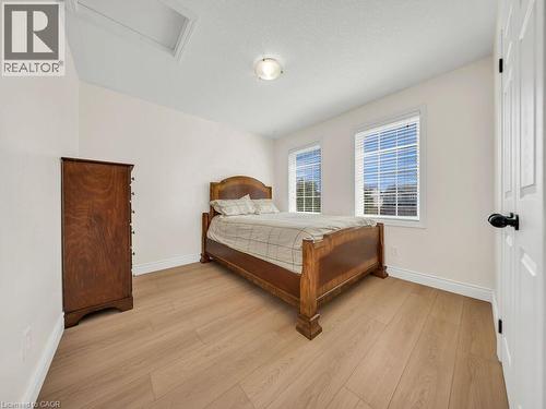 Light-filled room featuring two windows with horizontal blinds, light wood-finish flooring, a ceiling-mounted light fixture, and white trim - 39 Baintree Way, Cambridge, ON - Indoor Photo Showing Bedroom